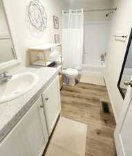 Full bathroom featuring toilet, shower / bath combo with shower curtain, vanity, and hardwood / wood-style flooring