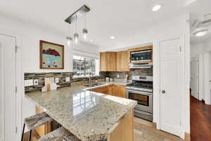 Kitchen with ventilation hood, stainless steel appliances, sink, decorative light fixtures, and light hardwood / wood-style flooring