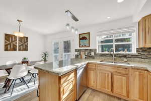 Kitchen featuring sink, stainless steel dishwasher, kitchen peninsula, light hardwood / wood-style floors, and decorative light fixtures