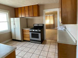 Kitchen with gas range oven, light tile patterned flooring, a textured ceiling, and white refrigerator