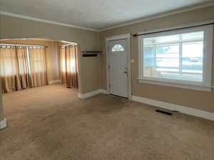 Carpeted entryway featuring a textured ceiling and ornamental molding