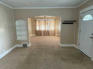 Entryway with light colored carpet, a textured ceiling, and ornamental molding