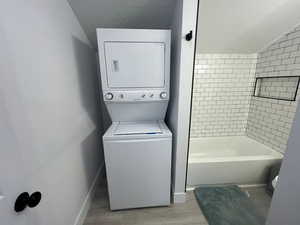 Laundry area with a textured ceiling, stacked washing maching and dryer, and light hardwood / wood-style floors