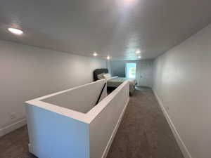 Corridor featuring a textured ceiling and dark colored carpet