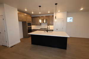 Kitchen featuring built in microwave, sink, an island with sink, pendant lighting, and oven