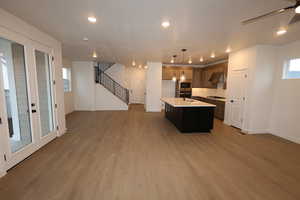 Kitchen with tasteful backsplash, decorative light fixtures, hardwood / wood-style floors, black gas stovetop, and a kitchen island with sink