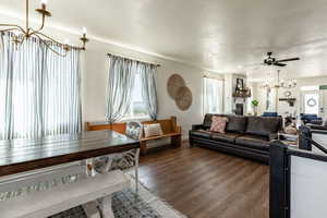 Living room with ceiling fan with notable chandelier and dark hardwood / wood-style flooring