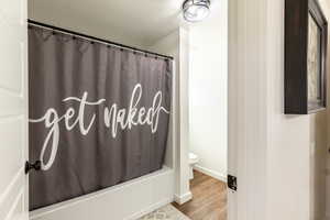 Bathroom with hardwood / wood-style floors, toilet, shower / bathtub combination with curtain, and a textured ceiling