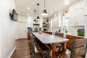 Kitchen with hanging light fixtures, white cabinetry, a center island, and dark wood-type flooring