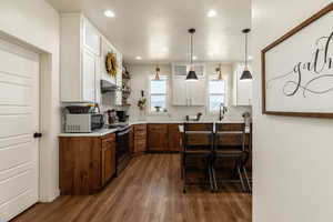 Kitchen featuring pendant lighting, a breakfast bar, stainless steel electric stove, white cabinets, and dark hardwood / wood-style floors