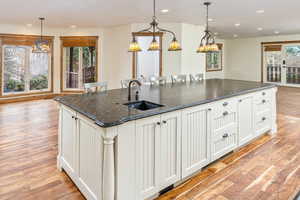 Kitchen with pendant lighting, light hardwood / wood-style floors, an island with sink, and dark stone counters