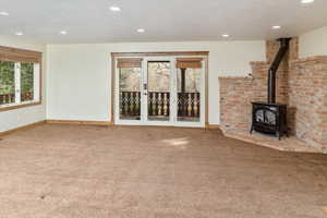 Unfurnished living room with a wood stove, light carpet, a healthy amount of sunlight, and a textured ceiling