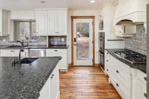 Kitchen with hardwood / wood-style floors, premium range hood, white cabinets, tasteful backsplash, and stainless steel appliances