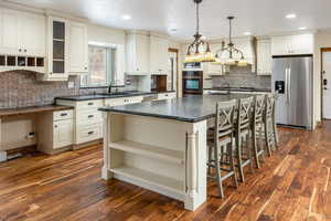 Kitchen with pendant lighting, dark wood-type flooring, a center island with sink, sink, and appliances with stainless steel finishes