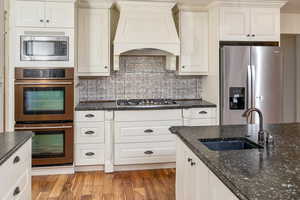 Kitchen featuring sink, dark wood-type flooring, stainless steel appliances, dark stone countertops, and custom range hood