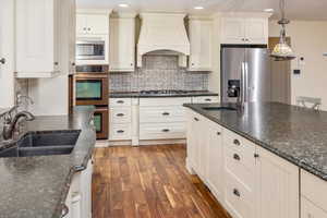 Kitchen featuring sink, dark hardwood / wood-style floors, premium range hood, decorative light fixtures, and appliances with stainless steel finishes