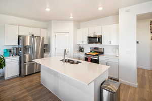 Kitchen with sink, white cabinetry, stainless steel appliances, and an island with sink