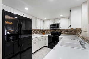 Kitchen featuring black appliances, backsplash, white cabinetry, and sink