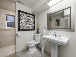 Bathroom featuring tile patterned floors, sink, a tile shower, and toilet