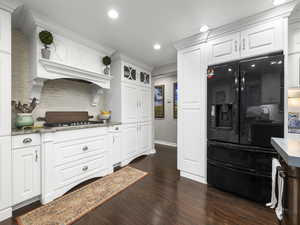 Kitchen with white cabinets, decorative backsplash, stainless steel gas stovetop, and black refrigerator with ice dispenser