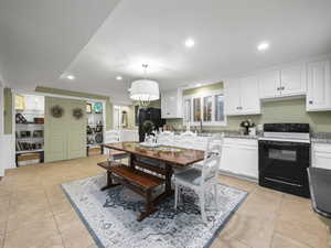 Kitchen featuring black appliances, decorative light fixtures, white cabinetry, and light tile patterned floors