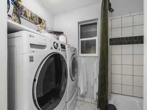 Clothes washing area featuring light tile patterned flooring and washer and dryer