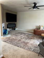 Carpeted living room with ceiling fan and a textured ceiling