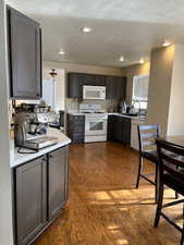 Kitchen featuring a textured ceiling, sink, white appliances, and dark wood-type flooring