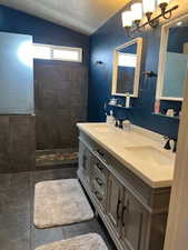 Bathroom with a tile shower, tile patterned floors, a chandelier, lofted ceiling, and vanity