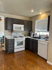 Kitchen featuring a textured ceiling, white appliances, sink, and dark wood-type flooring