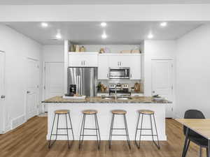 Kitchen featuring dark stone countertops, a kitchen island with sink, white cabinets, and appliances with stainless steel finishes