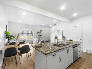 Kitchen featuring a kitchen island with sink, white cabinets, sink, stainless steel dishwasher, and light hardwood / wood-style floors