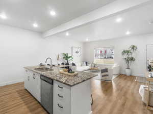 Kitchen featuring dishwasher, white cabinets, a center island with sink, sink, and light wood-type flooring