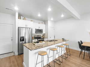 Kitchen with appliances with stainless steel finishes, a kitchen island with sink, sink, white cabinets, and light hardwood / wood-style floors