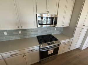 Kitchen with white cabinets, decorative backsplash, stainless steel appliances, and hardwood / wood-style flooring