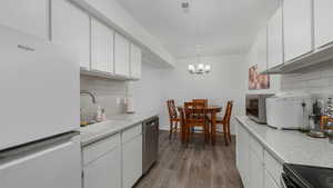 Kitchen featuring pendant lighting, backsplash, white cabinetry, and some stainless steel appliances