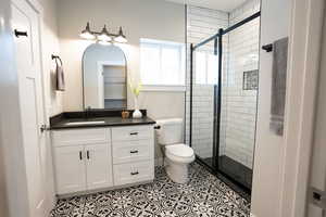 Bathroom with tile patterned floors, vanity, a shower with shower door, and toilet