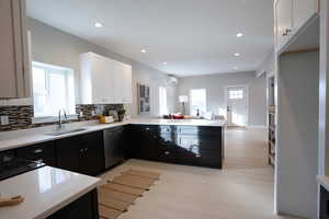 Kitchen with dishwasher, sink, kitchen peninsula, decorative backsplash, and white cabinetry