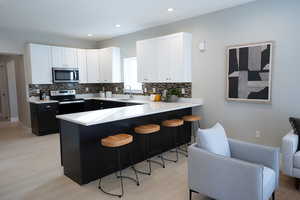 Kitchen featuring a breakfast bar area, kitchen peninsula, white cabinets, and appliances with stainless steel finishes