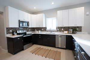 Kitchen with tasteful backsplash, stainless steel appliances, sink, light hardwood / wood-style floors, and white cabinetry