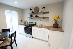 Kitchen featuring wooden counters, electric range, white cabinetry, and sink