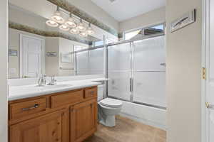 Full bathroom with tile floors, vanity, toilet, and enclosed tub / shower combo