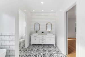 Bathroom with a bath, hardwood / wood-style floors, toilet, vanity, and tile walls