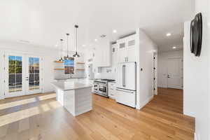 Kitchen with white cabinetry, premium appliances, light hardwood / wood-style floors, decorative light fixtures, and a kitchen island