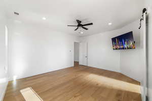 Empty room with a barn door, ceiling fan, and hardwood / wood-style flooring