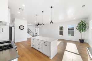 Kitchen with ceiling fan, a kitchen island, pendant lighting, white cabinets, and light wood-type flooring