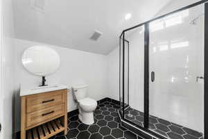 Bathroom featuring an enclosed shower, vanity, tile patterned flooring, toilet, and lofted ceiling