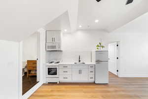 Kitchen with white cabinetry, sink, white appliances, and light wood-type flooring