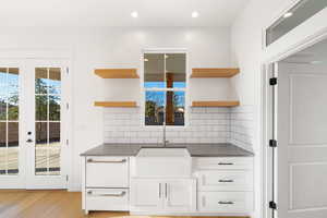 Kitchen with sink, french doors, tasteful backsplash, light hardwood / wood-style flooring, and white cabinets