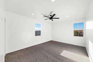 Spare room featuring dark colored carpet, ceiling fan, and a wealth of natural light